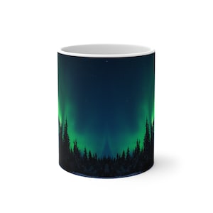 May include: A white ceramic mug with a design of a dark green aurora borealis over a silhouette of a forest. The aurora is a vibrant green with a dark blue background.
