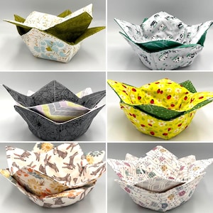 May include: A collection of six fabric bowl cosies featuring various patterns including floral, cow, ladybug, rabbit, and geometric designs. Each cosy has a square base with four pointed flaps extending upward, constructed from quilted fabric.