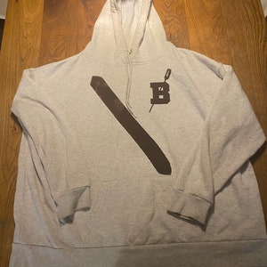Puede incluir: Una sudadera con capucha gris con una barra diagonal negra y una letra negra "B" con una aguja que la atraviesa.