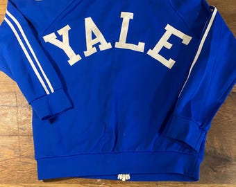 May include: A royal blue zip-up jacket with white stripes down the sleeves and the word "YALE" arched across the back in white block letters. The jacket has a ribbed hem and cuffs.