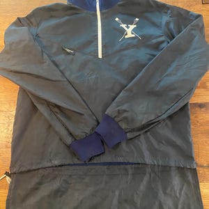 Puede incluir: Una chaqueta ligera de color azul oscuro con cierre de cremallera y tirador de cremallera blanco. La chaqueta tiene un cuello alto y un logotipo con la letra "Y" y dos remos cruzados detrás.