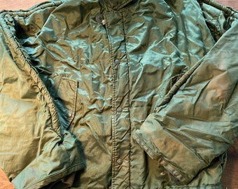 Puede incluir: Una chaqueta acolchada verde con cierre de presión y cintura con cordón. La chaqueta tiene un cuello alto y un bolsillo con cremallera en el pecho izquierdo.