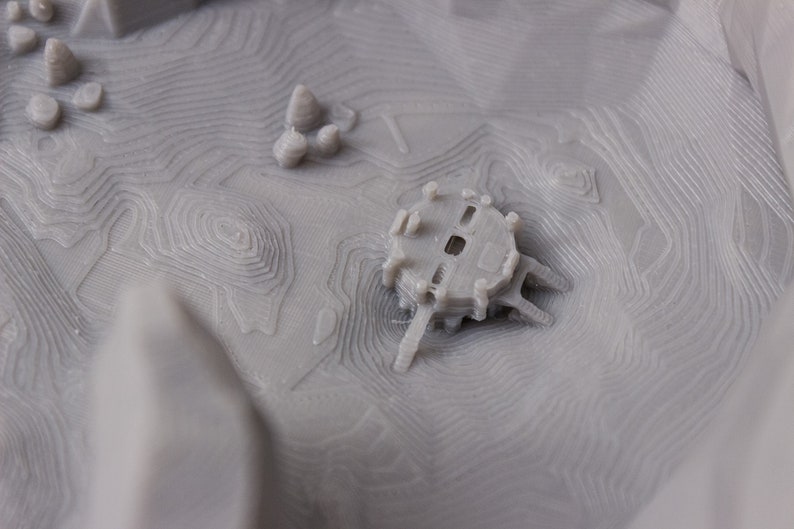 May include: A 3D printed model of a small building with a detailed design. The building is printed in a light gray color and has a textured surface.