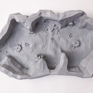 May include: A gray 3D printed terrain piece with a rocky, cratered surface. The piece is designed for use in tabletop games or miniature wargaming.