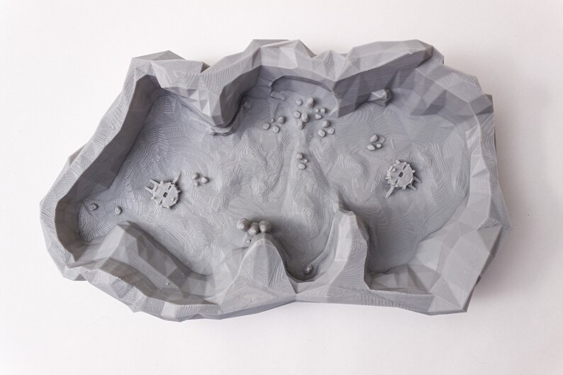 May include: A gray 3D printed terrain piece with a rocky, cratered surface. The piece is designed for use in tabletop games or miniature wargaming.