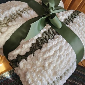 May include: A white and green striped throw blanket with a green satin ribbon tied in a bow. The blanket is made of a soft, fluffy material.