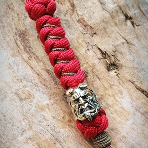 May include: Red and brown paracord keychain with a gold metal skull bead.