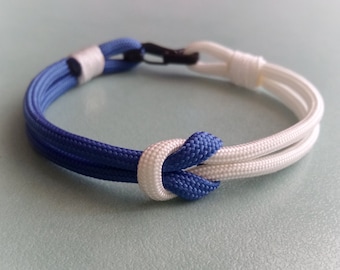 Op de afbeelding: Een blauw en wit paracord armband met een knoop in het midden.