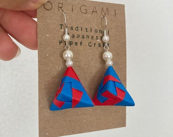 Könnte beinhalten: Origami-Ohrringe mit gewebten roten und blauen dreieckigen Anhängern. Jeder Ohrring hat einen silbernen Haken und ist mit drei weißen Kunstperlen verziert. Die Ohrringe werden auf einer braunen Karte mit dem Text "ORIGAMI Traditional Japanese Paper Craft" präsentiert.