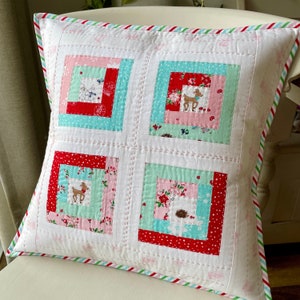 May include: A white cushion with a red, pink and blue patchwork design. The cushion has a green, white and red striped border. The patchwork design features a variety of small floral and animal prints.