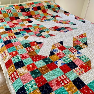 May include: A white quilt with a snowflake design. The quilt is made of colourful patchwork squares in shades of red, green, blue, yellow, and pink.