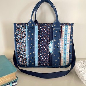May include: A patchwork tote bag with a navy blue background and various floral and star patterns. The bag has a shoulder strap and two handles. The bag is approximately 30 cm wide and 25 cm tall.