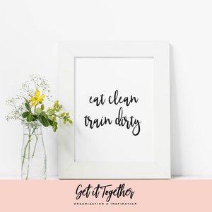 Peut inclure: Impression encadrée blanche avec une calligraphie noire qui dit "eat clean train dirty" avec un petit bouquet de fleurs jaunes dans un vase en verre transparent sur une surface rose. Le texte "Get it Together" est sous le cadre.