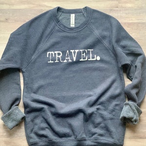 May include: A dark gray sweatshirt with the word "TRAVEL." printed in white on the front.