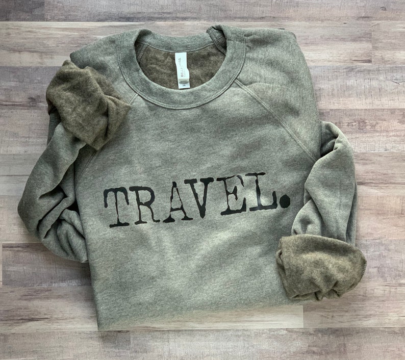 May include: A gray sweatshirt with the word "TRAVEL" printed in black on the front.