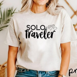 K&ouml;nnte beinhalten: Ein wei&szlig;es T-Shirt mit einer schwarzen Grafik, auf der "SOLO traveler" mit einem kleinen Flugzeug und einer Wolke steht.