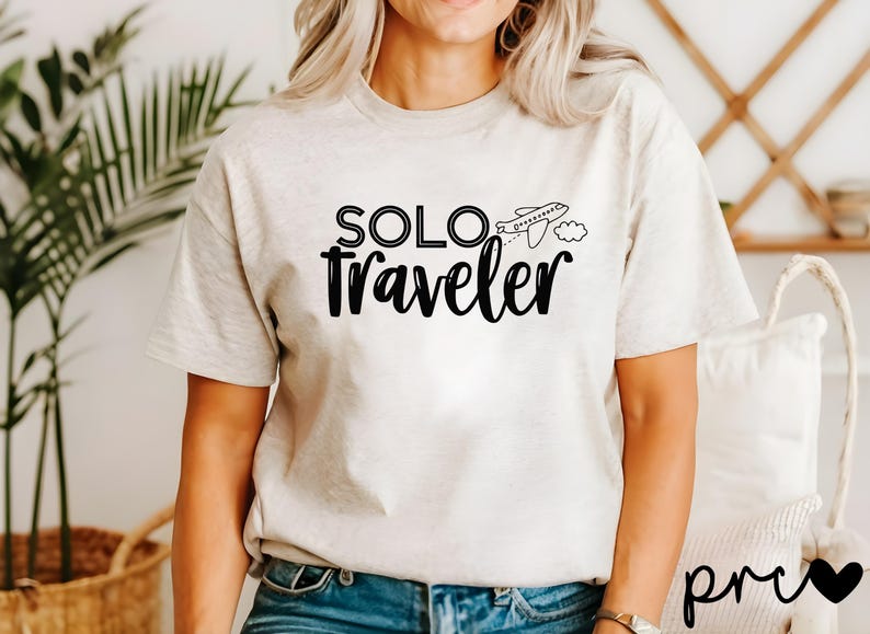 K&ouml;nnte beinhalten: Ein wei&szlig;es T-Shirt mit einer schwarzen Grafik, auf der "SOLO traveler" mit einem kleinen Flugzeug und einer Wolke steht.