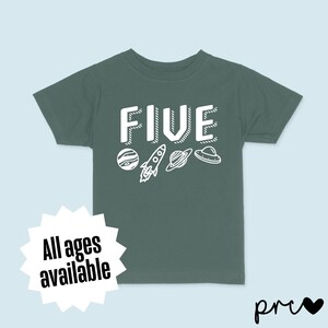May include: A dark green t-shirt with the word "FIVE" in white outlined letters. The shirt has a space theme with a rocket, planets, and a UFO.