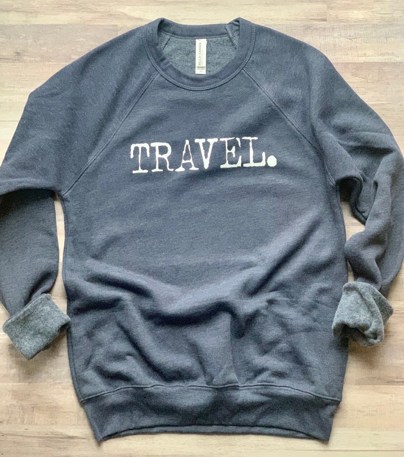 May include: A dark gray sweatshirt with the word "TRAVEL." printed in white on the front.