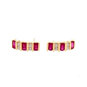 May include: A pair of gold stud earrings featuring a curved bar design. Each earring is set with three rectangular baguette-cut vibrant pink rubies alternating with two round brilliant-cut clear diamonds in a channel setting.