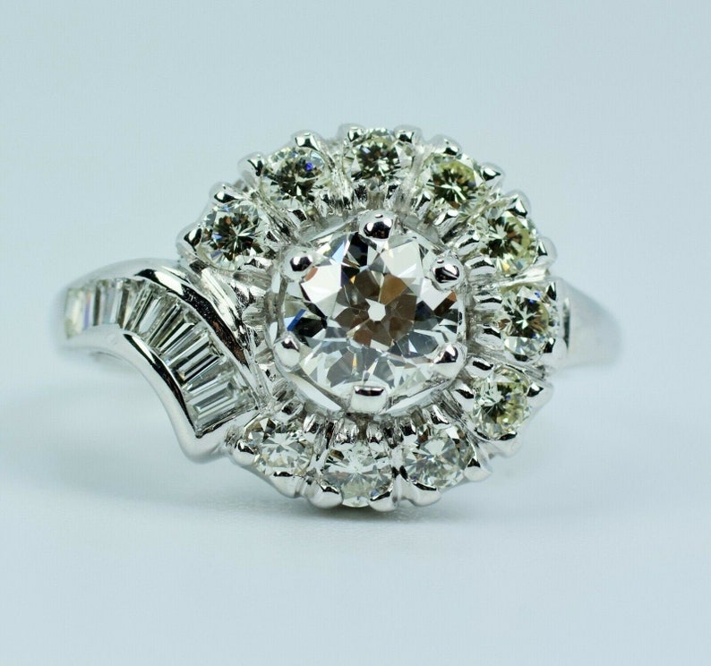 Pode incluir: Um anel de prata com um grande diamante redondo e claro rodeado por diamantes menores. A banda &eacute; adornada com diamantes em forma de baguette.