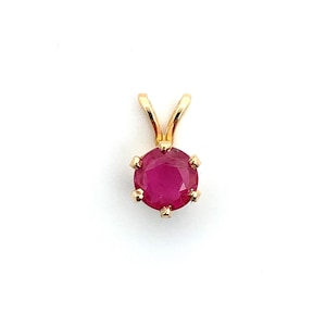 Könnte beinhalten: Ein goldener Anhänger mit einem runden, facettierten Rubin-Edelstein. Der Rubin hat eine tiefe, lebendige rote Farbe und ist in einer goldenen Lünette mit einem einfachen Bügel für eine Kette gefasst. Der Anhänger wird vor weißem Hintergrund gezeigt.