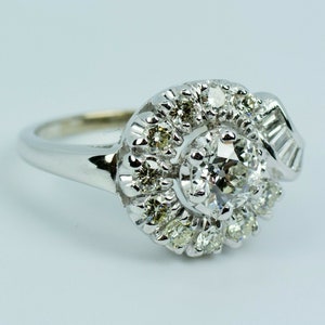 Pode incluir: Um anel de prata com um grande diamante redondo cercado por diamantes menores em espiral.
