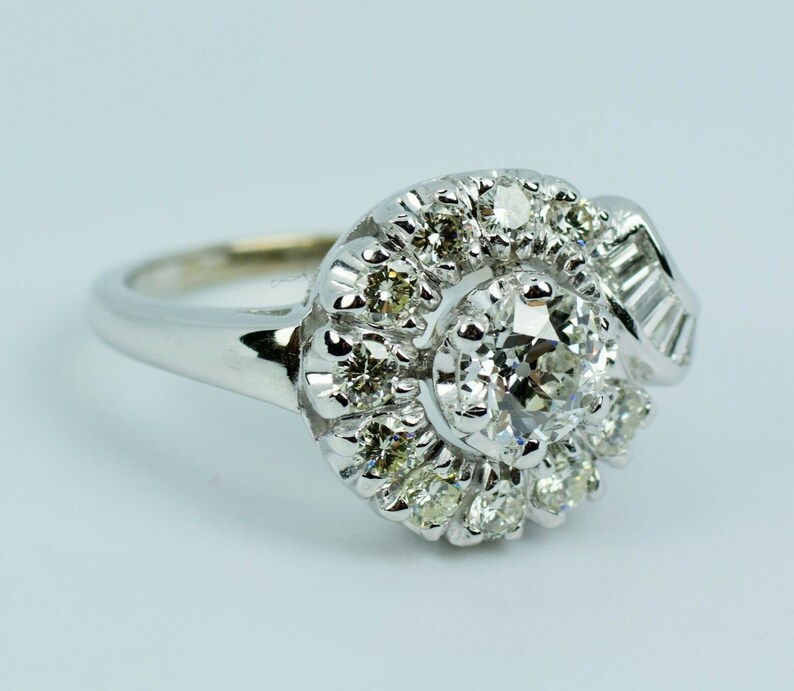 Pode incluir: Um anel de prata com um grande diamante redondo cercado por diamantes menores em espiral.