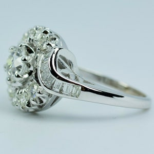 Pode incluir: Um anel de prata com um grande diamante redondo e claro cercado por diamantes menores. A banda &eacute; adornada com diamantes em forma de baguette.