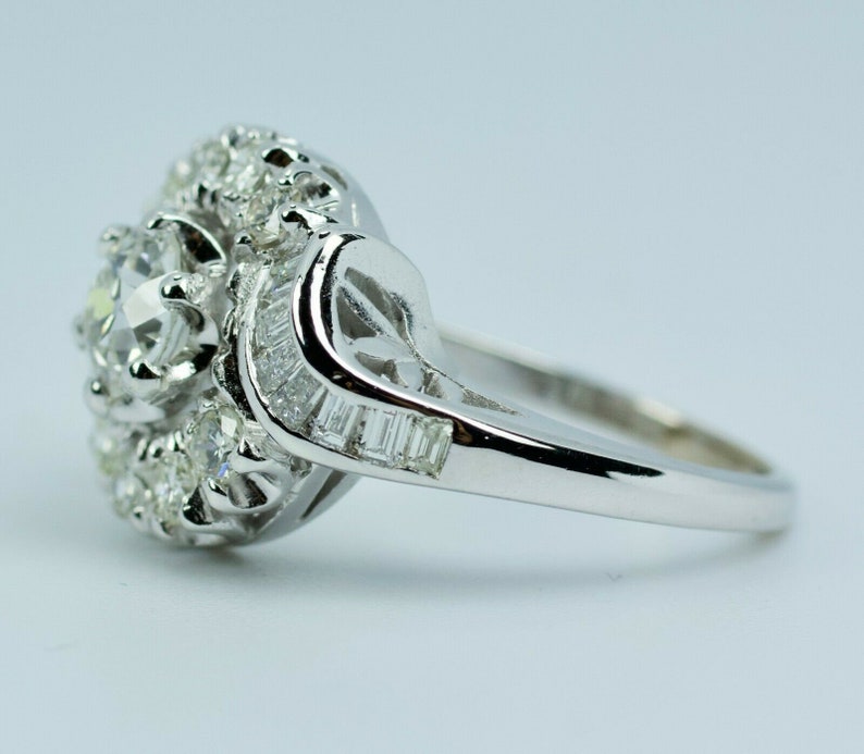 Pode incluir: Um anel de prata com um grande diamante redondo e claro cercado por diamantes menores. A banda &eacute; adornada com diamantes em forma de baguette.