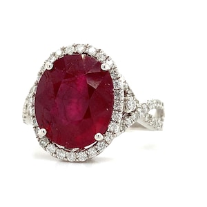 Peut inclure: Une bague éblouissante avec une grande pierre précieuse rubis de forme ovale. Le rubis est entouré d'un halo de petits diamants étincelants. Le bracelet de la bague a un design torsadé, également orné de diamants, créant un look luxueux et élégant.