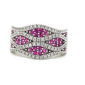 May include: A silver ring with a wave design, featuring alternating rows of small, round, bright pink gemstones and clear, sparkling white gemstones. The ring is set against a white background.