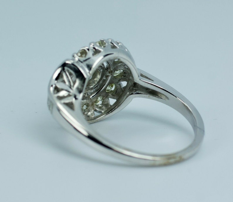 Pode incluir: Um anel de prata com um grupo de pequenos diamantes engastados em um design delicado e intrincado. O anel tem uma banda simples e uma parte superior arredondada.