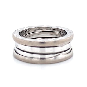 May include: A silver ring with a stacked design. The ring features a textured outer band and three smooth, polished bands. The ring is set against a white background.