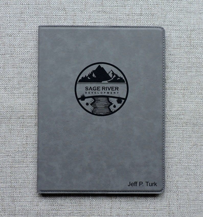 May include: Gray leatherette journal with a black logo of a mountain range and river with the text "Sage River Development". The name "Jeff P. Turk" is embossed in black at the bottom.