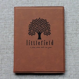 May include: Brown leather journal with a black tree and the text "littlefield... a place where kids can grow."