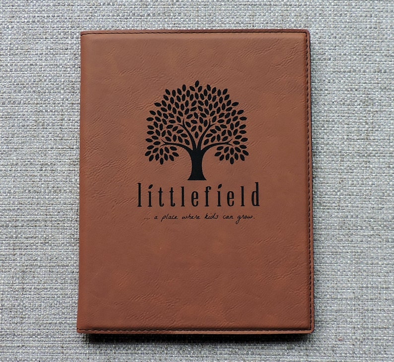 May include: Brown leather journal with a black tree and the text "littlefield... a place where kids can grow."