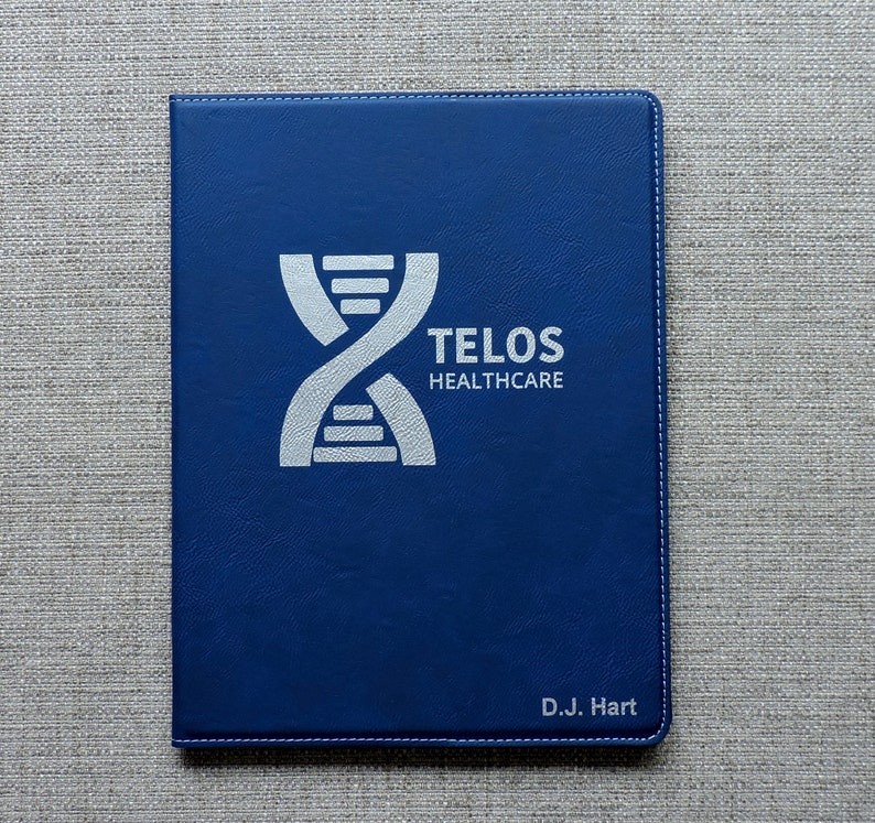 May include: A blue leather folder with a silver embossed logo that says "TELOS HEALTHCARE" and a DNA double helix symbol. The folder also has the name "D.J. Hart" embossed in silver at the bottom.