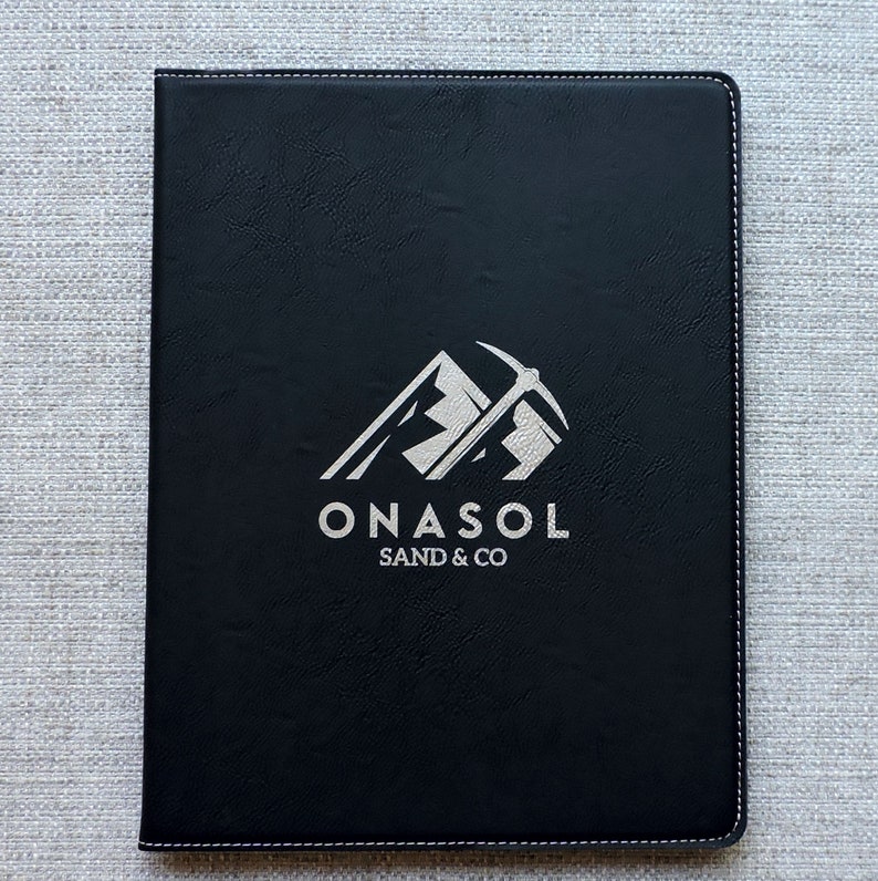 May include: Black leather folder with a silver embossed logo that says "ONASOL SAND & CO" and a graphic of a mountain with a pickaxe.