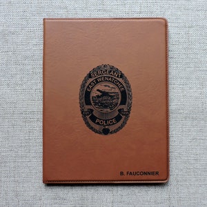 May include: A brown leather notebook with a black embossed police badge that reads "Sergeant East Wenatchee Police Est 1935" and the name "B. Fauconnier" at the bottom.