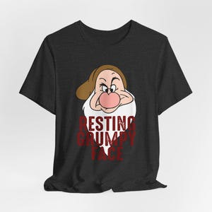 Könnte beinhalten: Ein anthrazitfarbenes Kurzarm-T-Shirt mit einer Grafik der Figur Grumpy, die einen braunen Hut trägt. Unter der Figur ist der Text RESTING GRUMPY FACE in einer abgenutzten roten Schrift gedruckt. Das Shirt hat einen Rundhalsausschnitt.