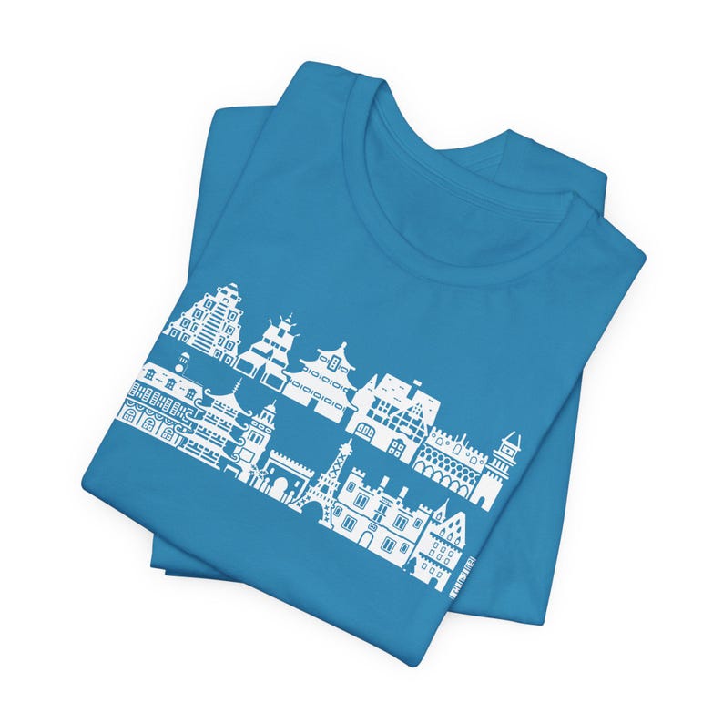 May include: A bright blue t-shirt featuring a white graphic print of various international architectural landmarks arranged in two horizontal rows, including towers, temples, and European-style buildings, centered on the front of the garment.