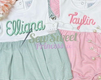May include: Two white baby onesies with striped bottoms. The onesies are personalized with the names "Elliana" in green and "Taylin" in pink.