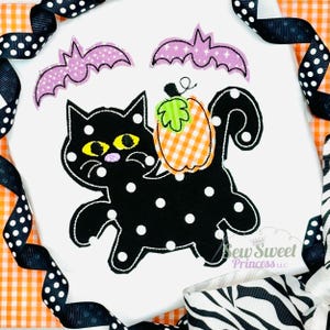 May include: A white Halloween-themed design featuring a black cat with white polka dots, holding an orange and white checkered pumpkin. Two purple bats are above the cat. The design is framed by black and white polka dot ribbon.