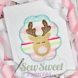 Op de afbeelding: Een witte romper met een roze, blauwe en groene gestreepte applicatie van een rendier met bruine geweien. De tekst "Sew Sweet Princess LLC" is onder de applicatie gedrukt.