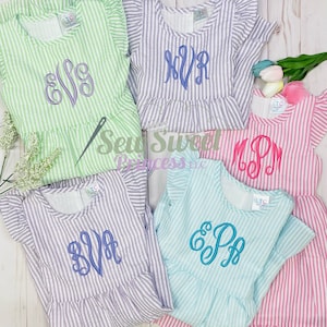 May include: Five striped dresses with different embroidered monograms. The dresses are in various colors, including green, purple, pink, blue, and white. The monograms are in different colors and styles.