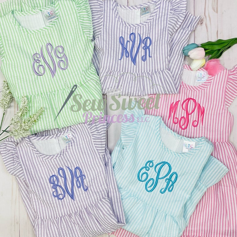 May include: Five striped dresses with different embroidered monograms. The dresses are in various colors, including green, purple, pink, blue, and white. The monograms are in different colors and styles.