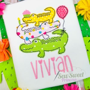 Op de afbeelding: Een witte romper met een stapel van drie geborduurde alligators, de bovenste draagt een cupcake-hoed en houdt een verjaardagskaars vast. De onderste alligator houdt een roze ballon met witte stippen vast. De naam "Vivian" is in roze onder de alligators geborduurd met hartjesaccenten. De tekst "Sew Sweet Princess LLC" is in roze onder de naam geborduurd.