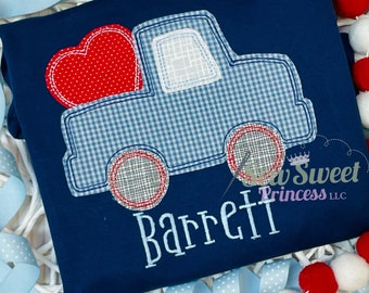 May include: Navy blue t-shirt featuring an embroidered design of a truck carrying a red heart. The truck has a blue and white gingham pattern. The name "Barrett" is embroidered in white script below the truck.