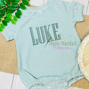 May include: A green and white striped baby onesie with the name "LUKE" embroidered on the front.